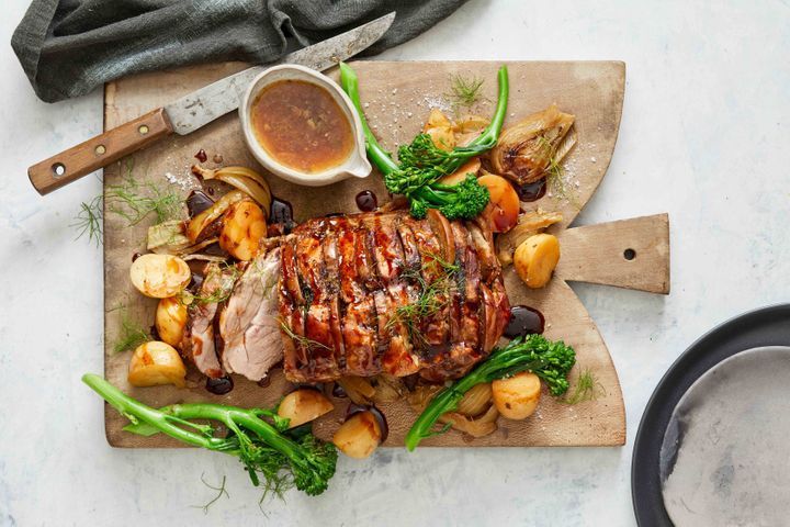 A rustic platter with slow-roasted pork belly surrounded by caramelised apple slices and fresh herbs
